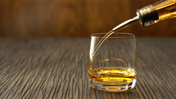 Gieten van whisky in het glas op een houten tafel - Foto, afbeelding