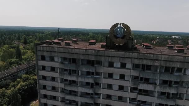 Abandonado edifício de vários andares com o brasão de armas soviético na fachada na cidade morta de Pripyat. Cidade fantasma na zona de Chernobyl
. - Filmagem, Vídeo