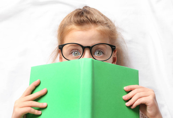 Cute girl with book lying on white sheets - Fotografie, Obrázek