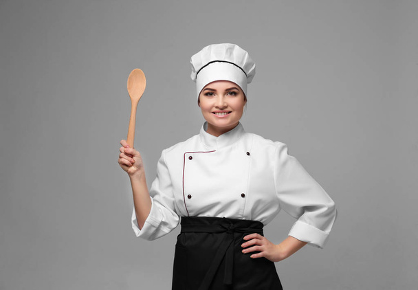 Portrait of young woman chef with wooden spoon on light background - Foto, afbeelding