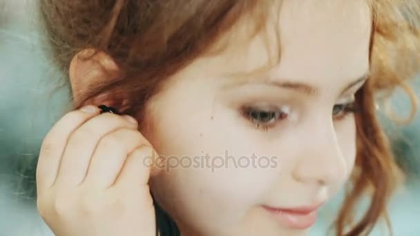 Image of pretty little girl looking in mirror and putting on earrings. close-up view. - Video