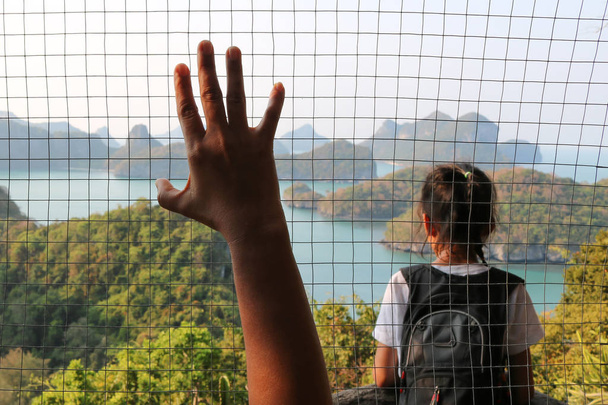 Mano sosteniendo la malla de acero y la niña con la vista de la isla tanga ang
. - Foto, imagen