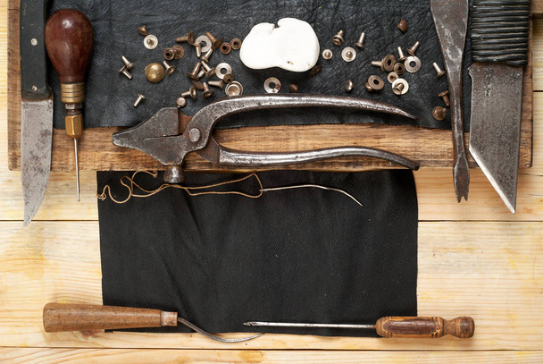 Leder-Bastelwerkzeuge auf Holz-Hintergrund. Handwerkertisch. Fell und handgefertigte Werkzeuge. Ansicht von oben - Foto, Bild