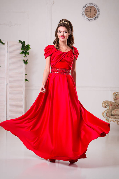Elegant woman in a long red dress is standing in a white room, dress swirl - Foto, immagini