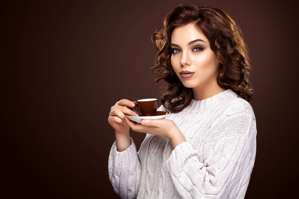 beautiful young woman with a cup of coffee standing on the brown background - Photo, Image