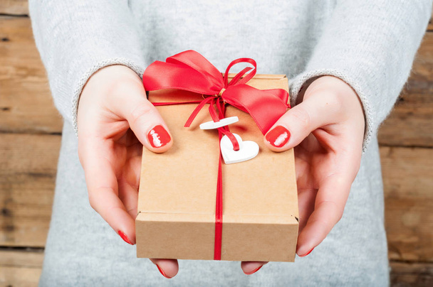 Hands holding gift in kraft box on a wooden background. The conc - Foto, Imagen