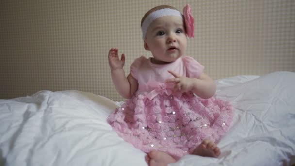 krásná holčička v růžových šatech sedící na posteli - Záběry, video