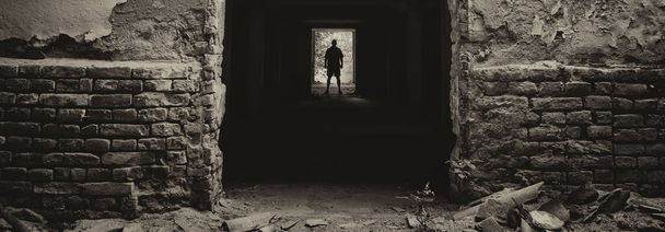 Silhouette of the man standing at the end of dark corridor of abandoned building - Photo, Image