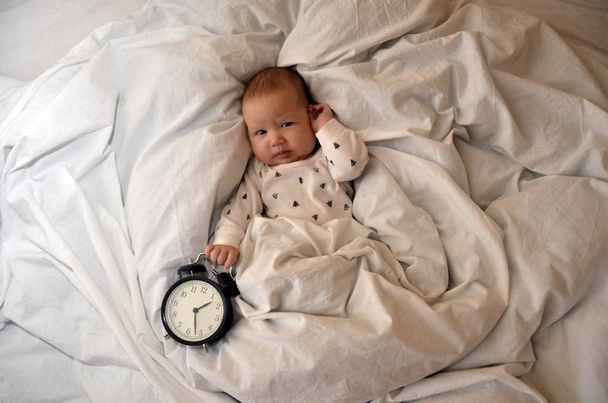 Kind mit Wecker auf dem Bett liegend und wünscht allen einen guten Morgen. Zeit zum Arbeiten. Zeit zum Schlafen. von oben - Foto, Bild