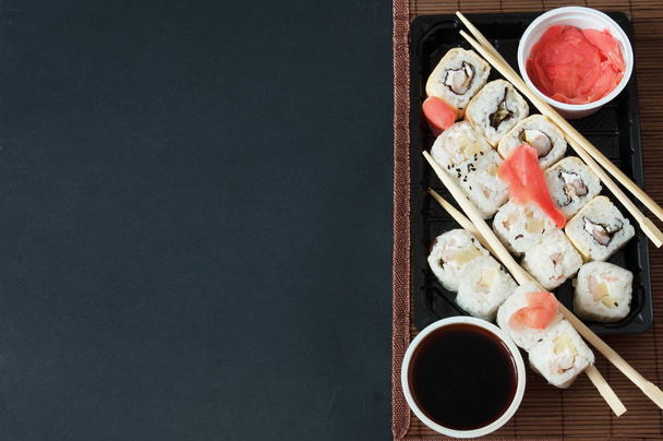 verschiedene Arten von Sushi-Rollen auf schwarzem Hintergrund serviert. Sushi zum Mitnehmen - Foto, Bild