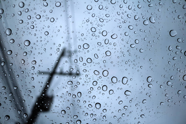 Regentropfen auf Glas mit blauem Himmel und Lichtmasten. - Foto, Bild