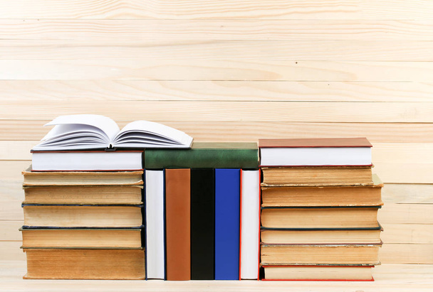 Open book, stack of hardback books on wooden table. - Foto, Bild