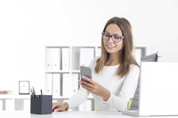 Beautiful woman in glasses with phone in office - Foto, imagen