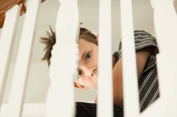 Boy looking scared through the handrail of a staircase - Photo, Image