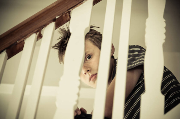 Boy looking scared through the handrail of a staircase - Photo, Image