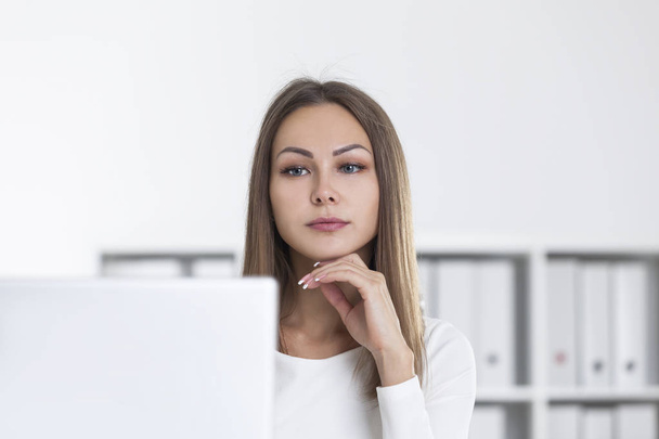 Pensive woman in white office looking at screen - Photo, image