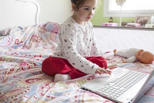 Petite fille assise au lit et surfant sur Internet dans sa chambre
 - Photo, image