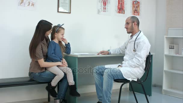 Pediatrician doctor examining child, while mother holding babygirl in her arms - Πλάνα, βίντεο