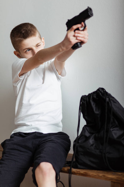Jonge jongen zittend op een bankje een pistool omhoog - Foto, afbeelding