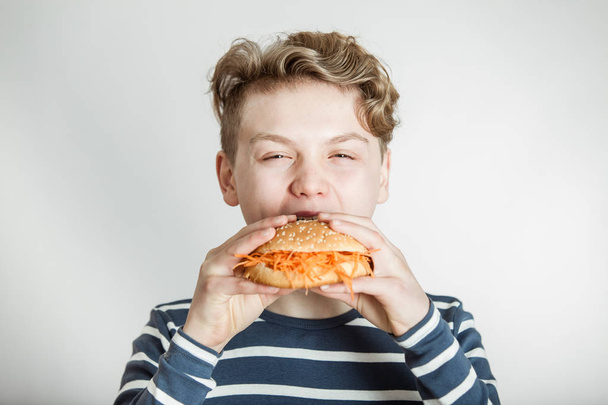 Хлопчик їсть гамбургер булочки увінчаний подрібнених морква - Фото, зображення