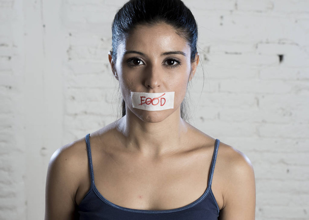 primer plano cara de joven hermosa mujer latina triste con la boca sellada en cinta adhesiva con el texto sin comida
 - Foto, imagen