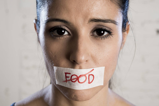 close up face of young beautiful sad latin woman with mouth sealed on stick tape with the text no food - Фото, изображение