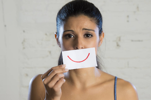 junge schöne depressive Frau, die ihre Trauer hinter einem Papier mit einem gezeichneten Lächeln versteckt - Foto, Bild