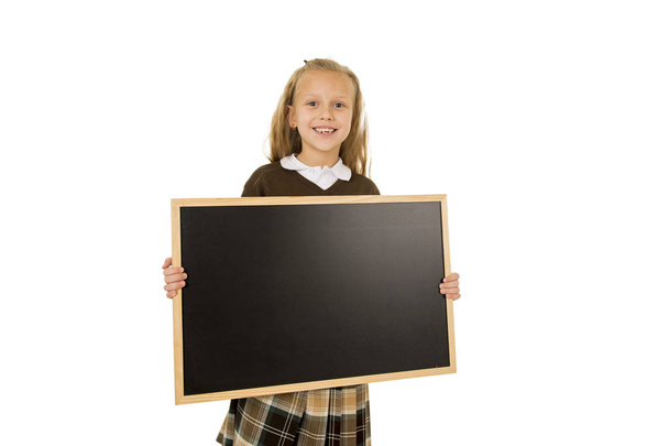 kleine schöne blonde Schulmädchen lächelt glücklich und fröhlich halten und zeigt kleine leere Tafel - Foto, Bild