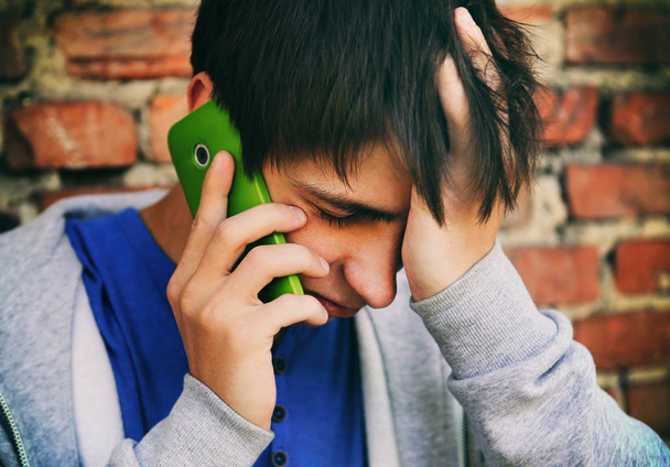 Trieste jongeman met een telefoon - Foto, afbeelding