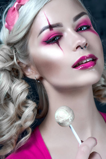 Mooie blonde meisje met twee pigtails, met creatieve pop make-up: roze glanzend lippen, het dragen van roze skelet jurk likken lollipop. voor de Halloween-party. Close-up, geretoucheerde foto. - Foto, afbeelding