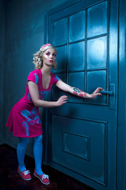 Beautiful blonde girl with two pigtails, with creative doll make-up: pink glossy lips, wearing pink skeleton dress, posing near the door. for the Halloween party. Posing like a doll. Studio shot, reto - Photo, Image