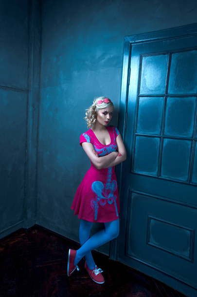 Beautiful blonde girl with two pigtails, with creative doll make-up: pink glossy lips, wearing pink skeleton dress, posing near the door. for the Halloween party. Posing like a doll. Studio shot, reto - Photo, Image