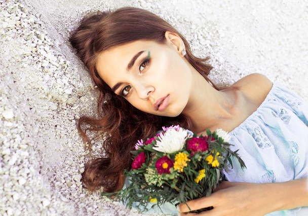 Beautiful young woman with delicate flowers in her hands. Closeup fashionable portrait of girl with elegant makeup. Pretty girl with bouquet of flowers looking at camera. - Foto, Bild