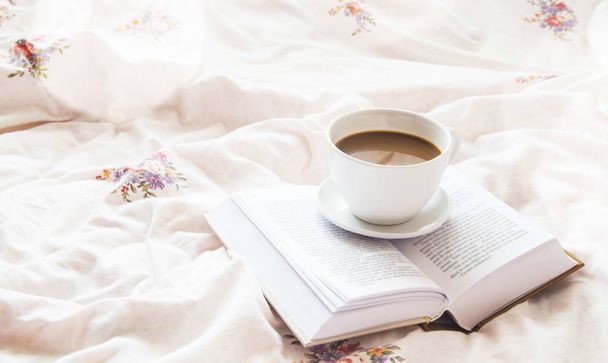 Натюрморт чашка кави і книга в ліжку на квіткових простирадлах
 - Фото, зображення