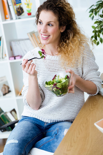 Beautiful young woman eating salad at home. - 写真・画像