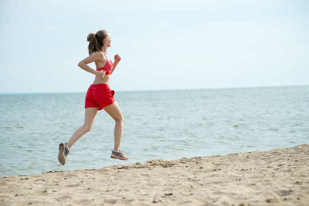 Young lady running at the sunny summer sand beach. Workout.  Jog - Foto, Imagem