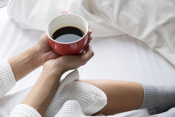 Pihentető fiatal nő élvezi a kávéját, míg ült az ágyban. - Fotó, kép