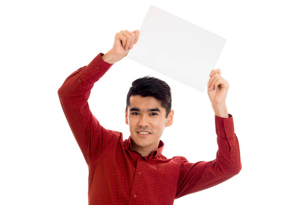 young cheerful brunette man in red t-shirt posing with white placard isolate on  background - Fotó, kép