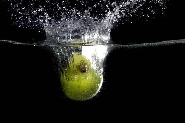 Зелене яблуко падає у воду з бризкою на чорному тлі
 - Фото, зображення