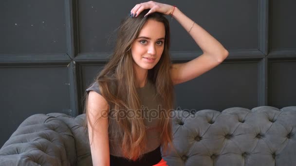 Beautiful girl in dress is sitting on the soft gray couch - Imágenes, Vídeo