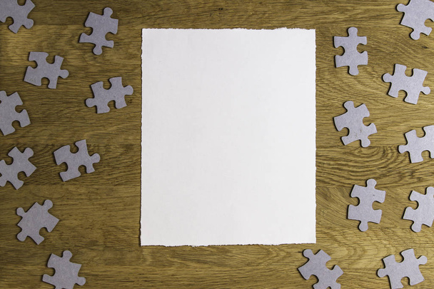 White torn paper piece surrounded by puzzle pieces on wooden background. Top view. Copy space for text - Photo, Image
