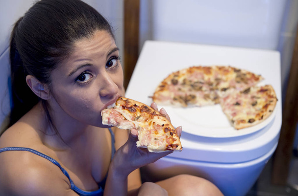 donna bulimica sentirsi male seduto sul pavimento del bagno appoggiato al WC mangiare pizza
 - Foto, immagini