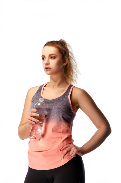 Beautiful young model with a bottle of water looks into the distance. Blonde woman in sportswear in the studio. Strong and attractive professional athlete. Girl with a ponytail. - Photo, Image