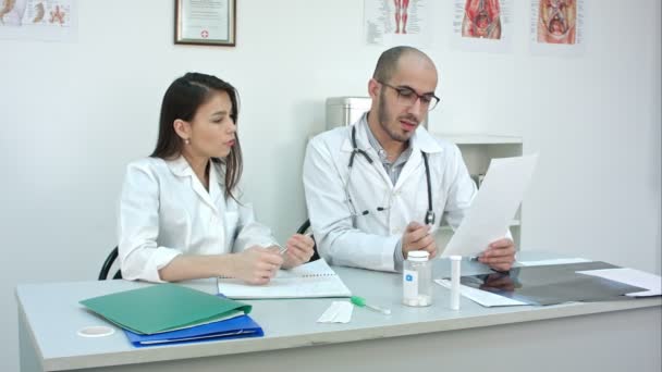 Doctor showing his female trainee how to read cardiogram while she making notes - Filmati, video
