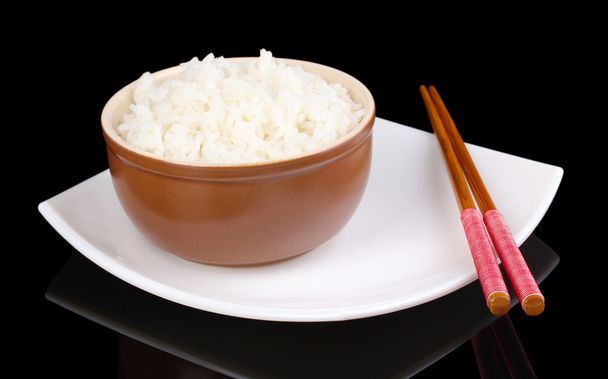 Schüssel Reis und Essstäbchen auf Teller isoliert auf schwarz - Foto, Bild