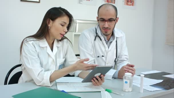 Pretty young nurse showing something on the tablet to her male colleague - Footage, Video