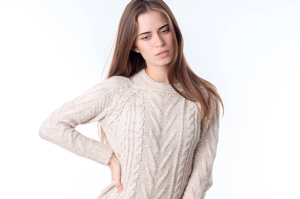 young girl in white sweater keeps her hand on the side and looks down - Foto, imagen