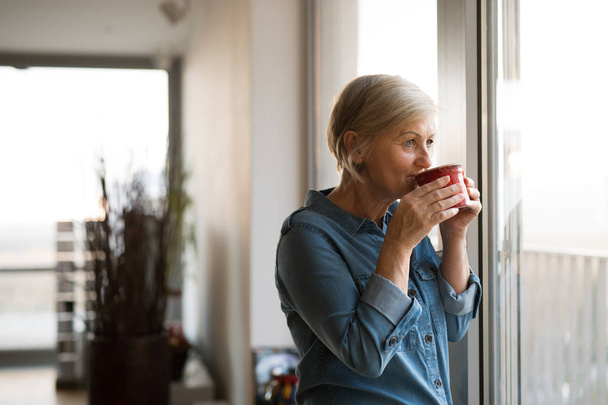 Senior woman at the window holding a cup of coffee - Foto, Imagem