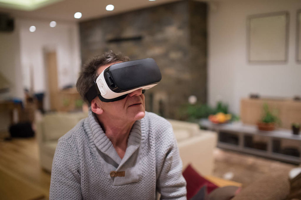 Senior man wearing virtual reality goggles at home - Foto, Imagem