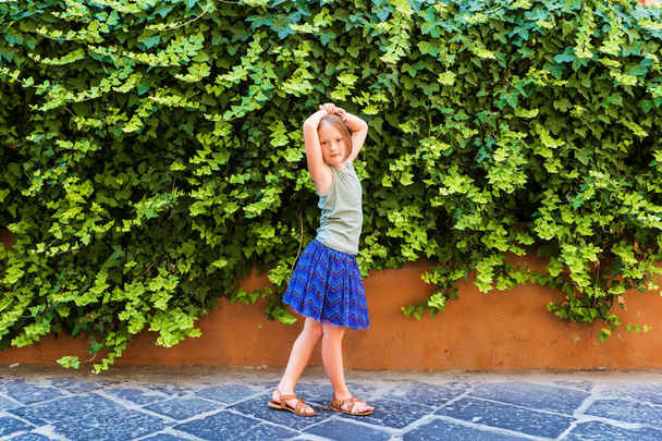 Sommermode für Kinder, Outdoor-Porträt eines niedlichen kleinen Mädchens mit blauem Rock, grünem Oberteil und lederbraunen Schuhen - Foto, Bild